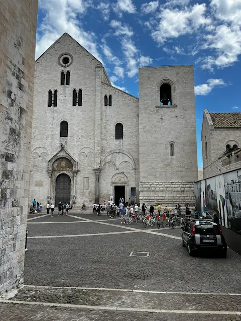 Facade of Basilica di San Nicola in Bari with people and cyclists in the piazza