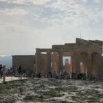 Visitors walking through the Propylaea on the Acropolis hill in Athens, Greece, with dramatic sky in the background.