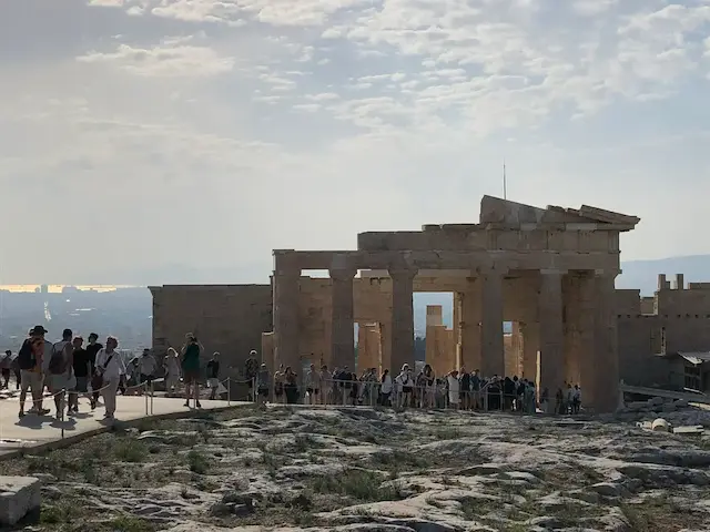 Visitors walking through the Propylaea on the Acropolis hill in Athens, Greece, with dramatic sky in the background.