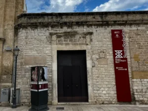 Stone entrance of Museo Archeologico di Santa Scolastica in Bari with modern red signage